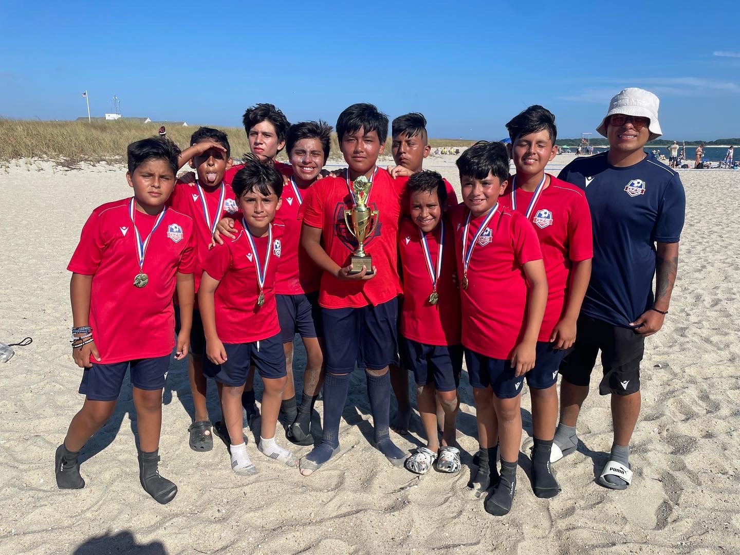 Young players holding a trophy and medals at a beach tournament