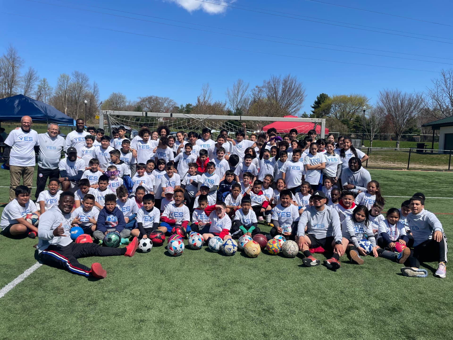 A large group of YES players and coaches in white YES shirts on the soccer field